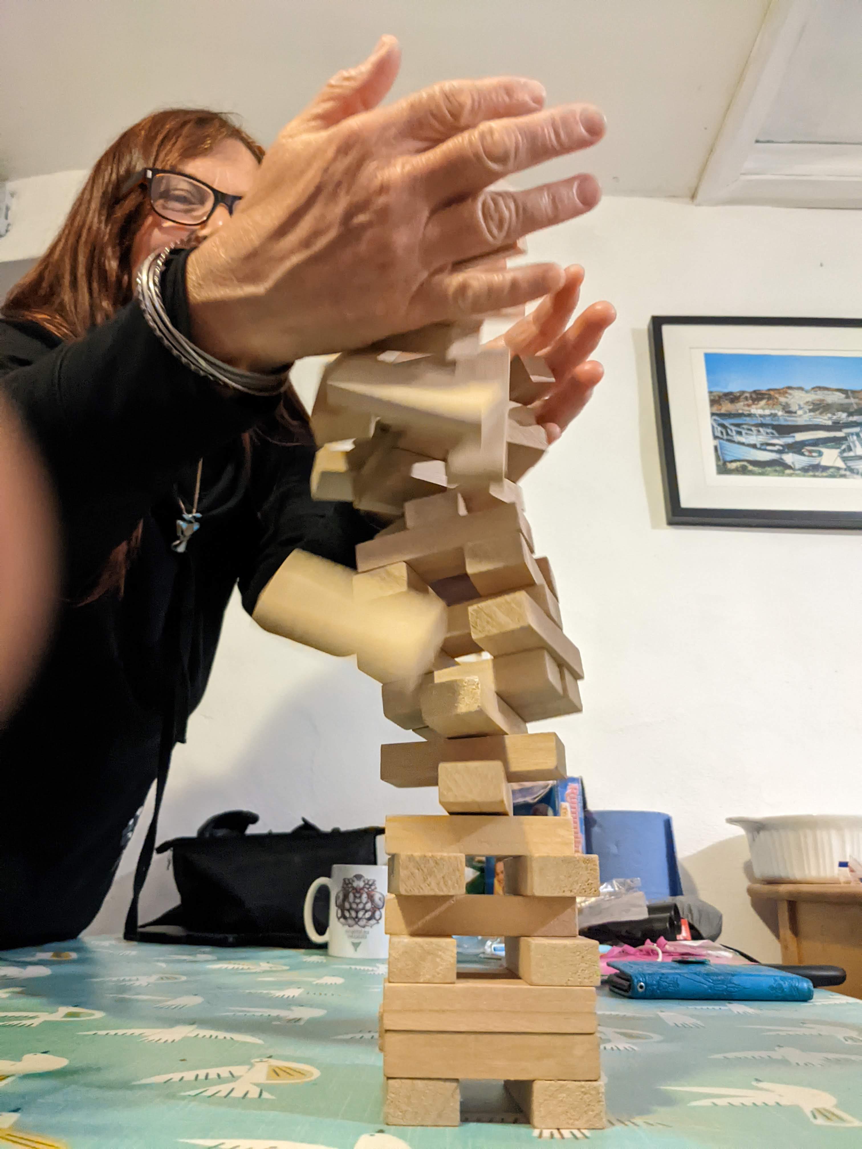 A jenga tower mid-fall with someone holding their hands around it